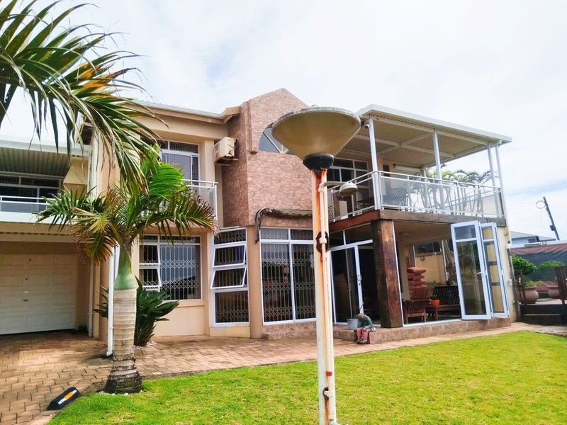Rear view of a multi-story house featuring a covered patio, balcony with glass balustrades, and a landscaped garden area.