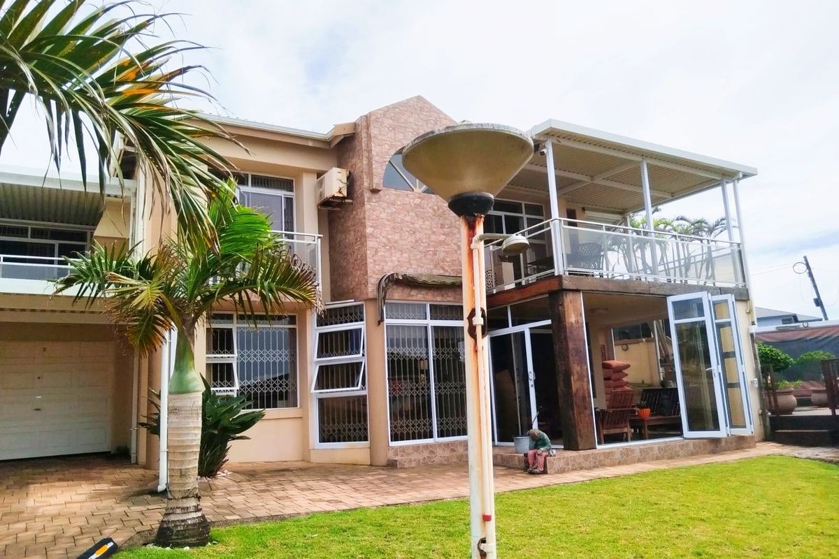 Rear view of a multi-story house featuring a covered patio, balcony with glass balustrades, and a landscaped garden area.