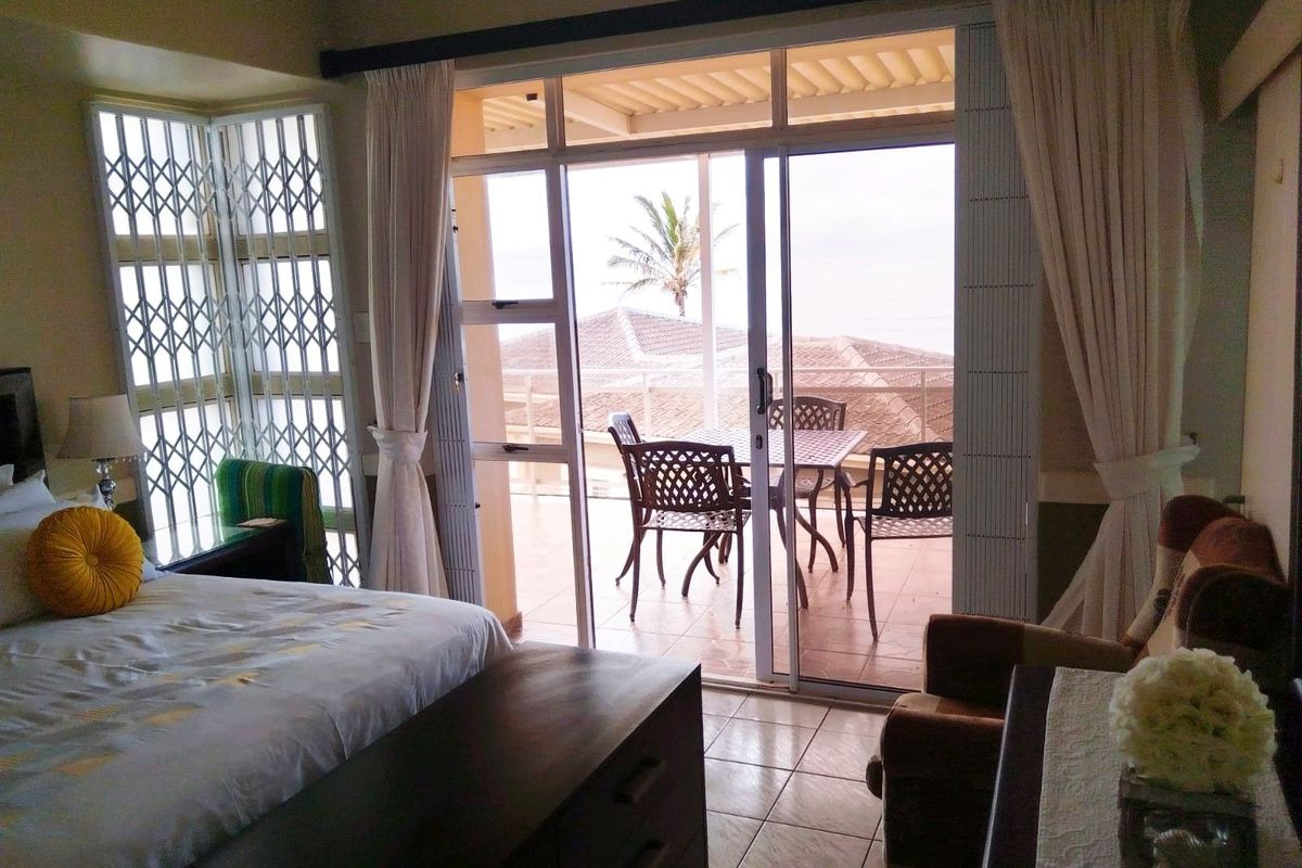 A bedroom featuring tiled flooring and sliding glass doors that open onto a private balcony with coastal views and security gates.
