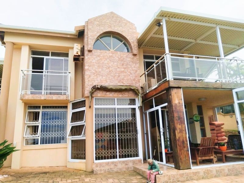 Rear view of a multi-level house featuring a stone-clad facade, glass balconies, sliding doors with security gates, and a covered patio area.