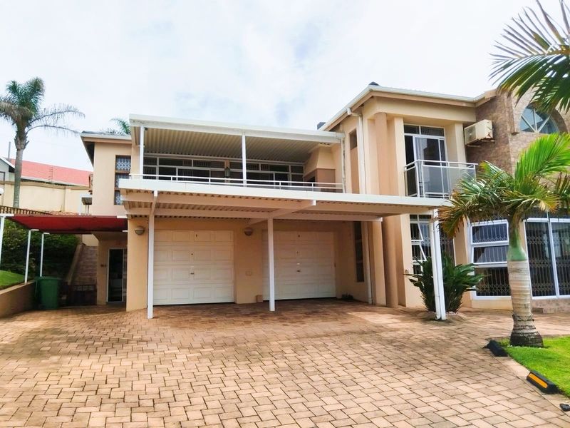 Front elevation of a multi-story house featuring a double garage, paved driveway, and a covered balcony area.