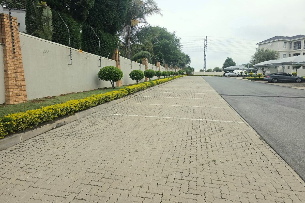 A well-maintained paved parking area within the apartment complex, featuring perimeter walling with electric fencing and landscaped garden borders.
