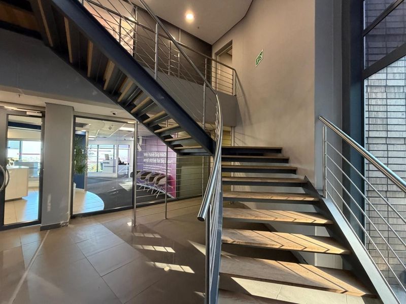 Modern office entrance featuring an open-tread staircase with stainless steel balustrades, glass partitioning, and clean tiled flooring in a professional commercial setting.