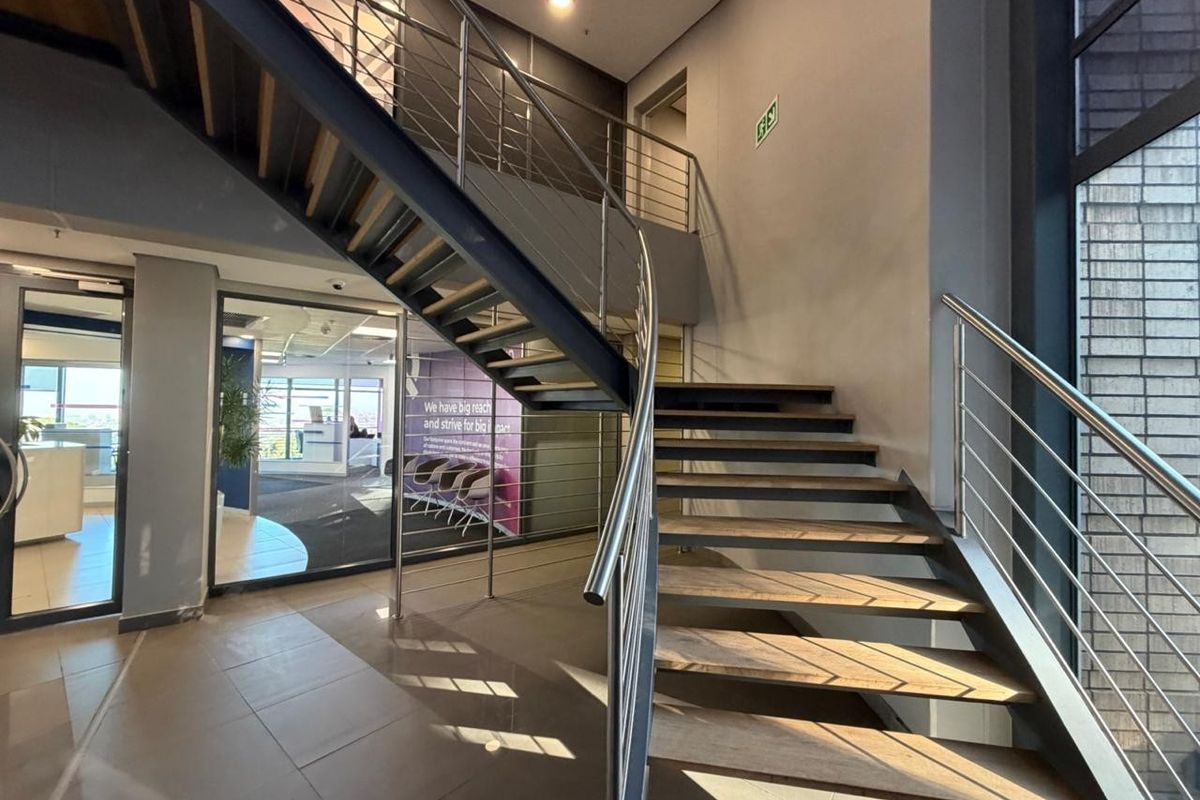 Modern office entrance featuring an open-tread staircase with stainless steel balustrades, glass partitioning, and clean tiled flooring in a professional commercial setting.