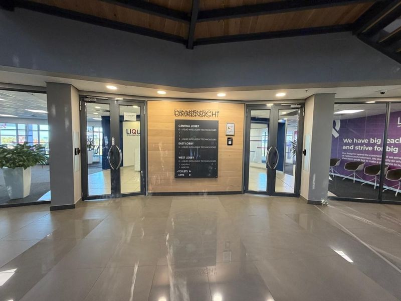 Modern office building entrance lobby featuring glass double doors, directory signage, and polished tiled flooring with timber accent wall paneling.