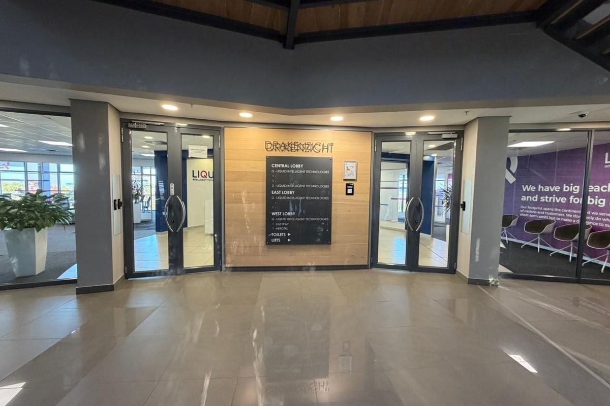 Modern office building entrance lobby featuring glass double doors, directory signage, and polished tiled flooring with timber accent wall paneling.