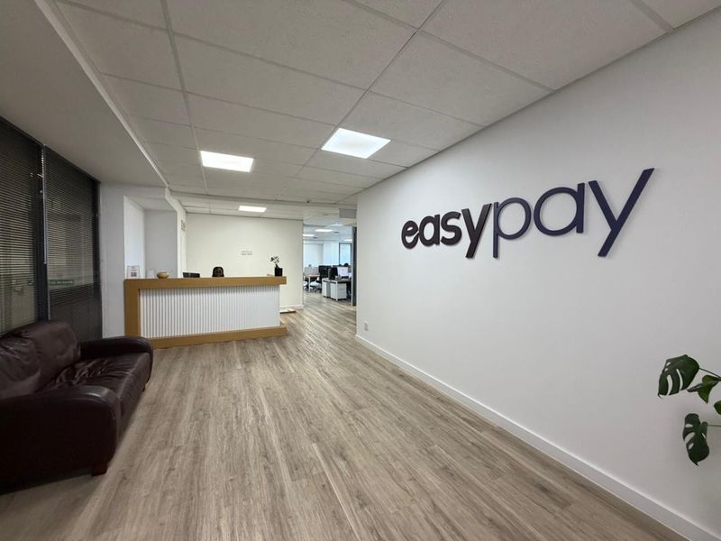 Professional office reception area featuring a built-in reception desk, modern laminate flooring, and a clean, bright suspended ceiling with recessed lighting.