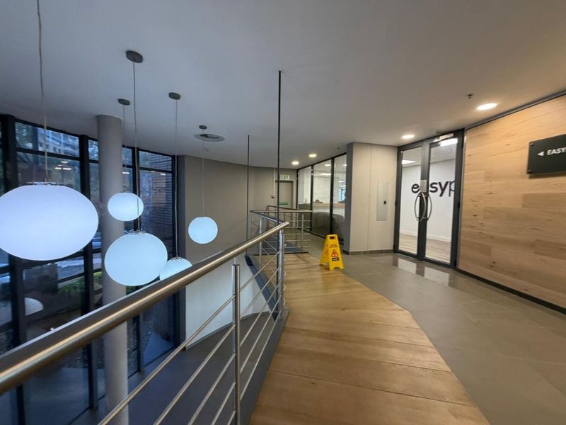 Modern office hallway featuring a stainless steel balustrade, glass partitions, and a wood-paneled feature wall with contemporary pendant lighting.