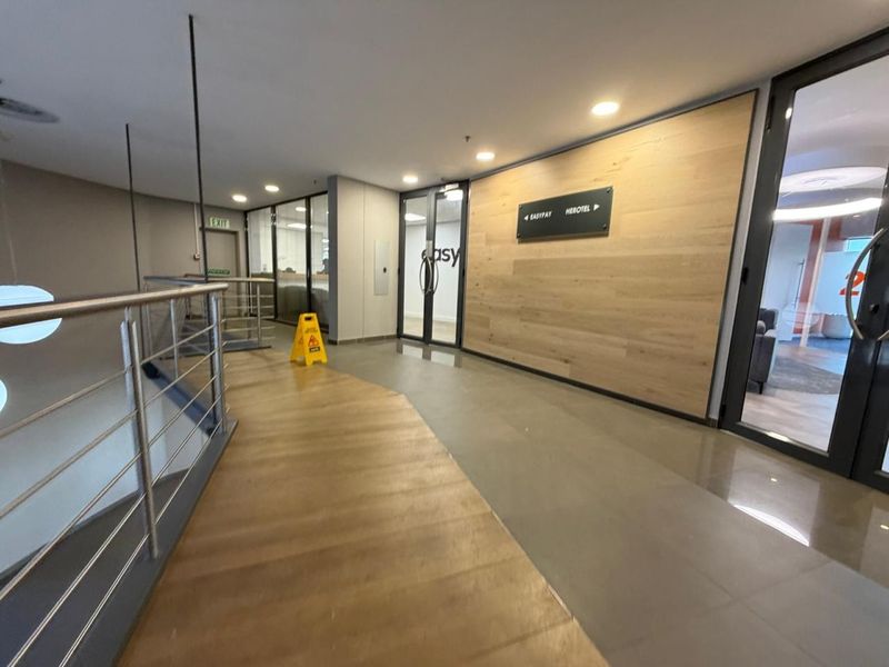 Modern office building hallway featuring wood-look wall paneling, stainless steel balustrades, and glass-paneled office doors with directional signage.