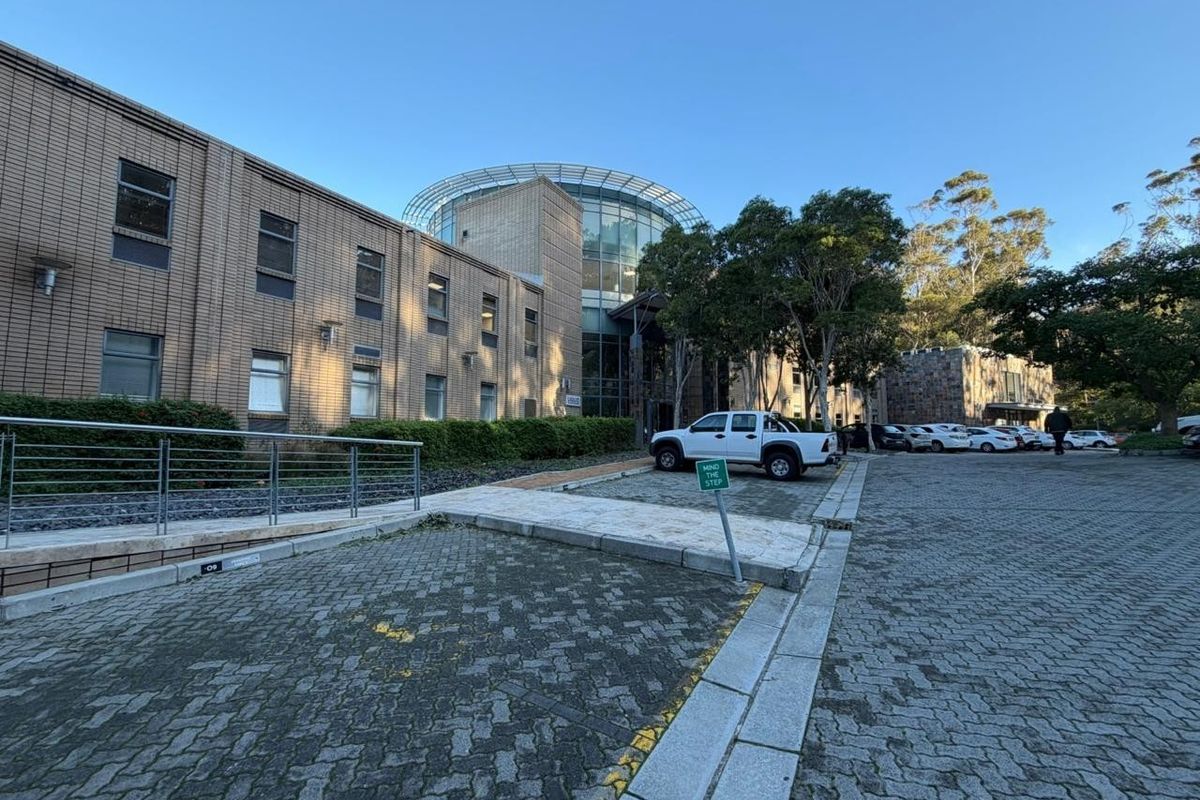Exterior view of a multi-story office building featuring a brick facade, glass architectural elements, and an adjacent paved parking area.