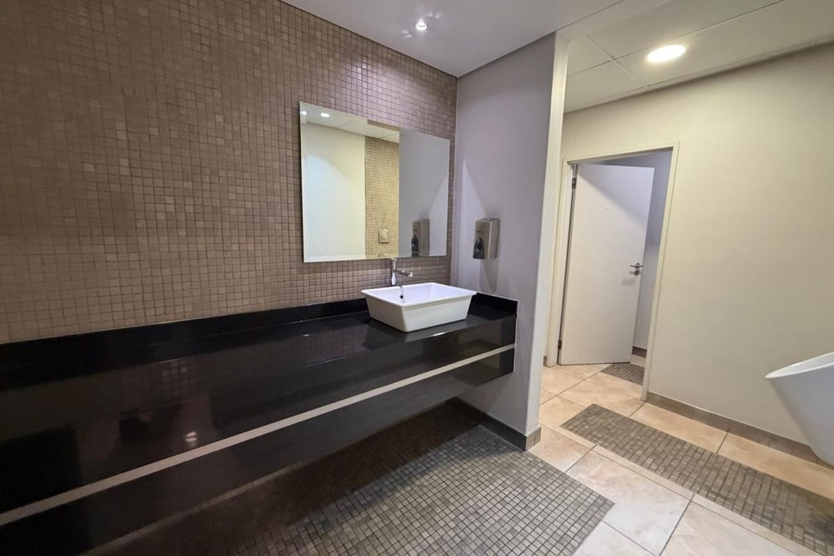 A clean, modern office bathroom featuring a sleek black vanity countertop, vessel sink, mosaic tile backsplash, and recessed lighting.