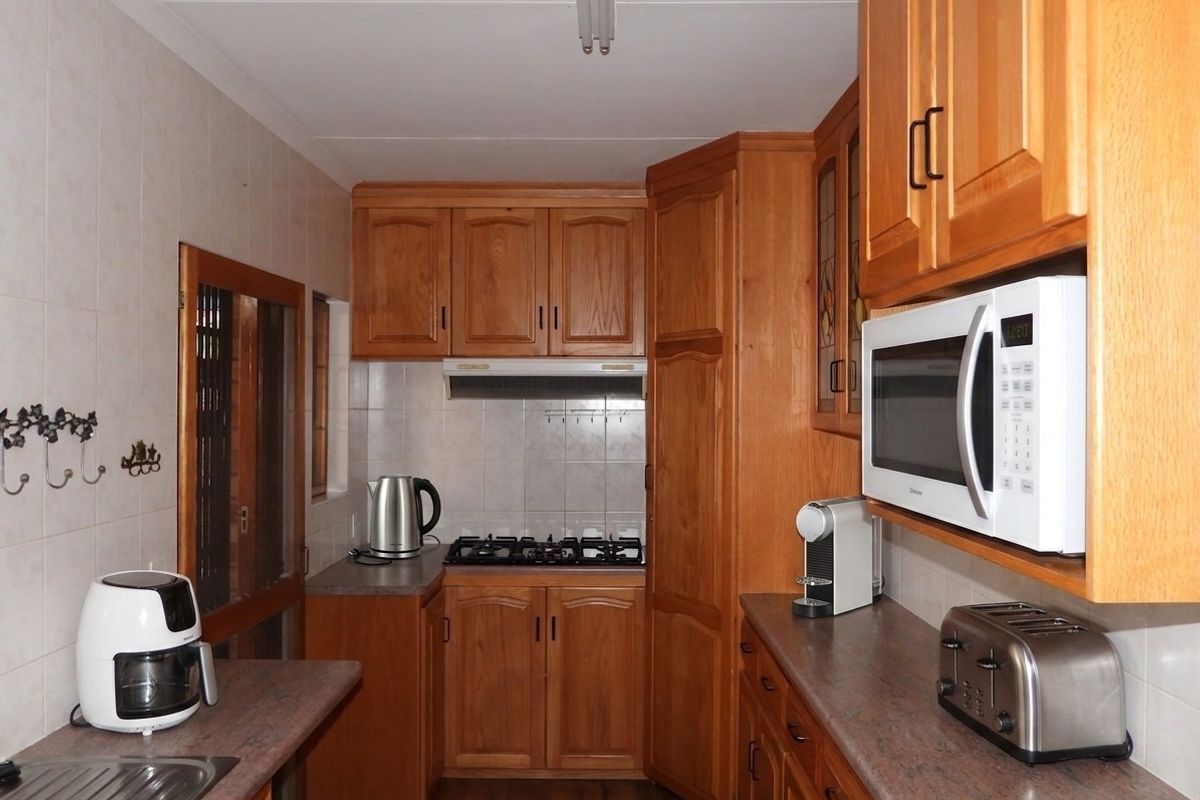 A functional kitchen featuring timber cabinetry, laminate countertops, a built-in gas hob, and an integrated microwave, offering a classic and practical workspace.