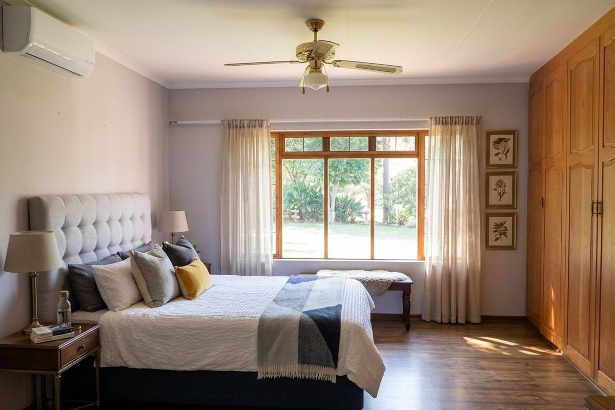 A well-maintained bedroom featuring wood-look flooring, built-in wooden cabinetry, a ceiling fan, and a wall-mounted air conditioning unit with garden views.