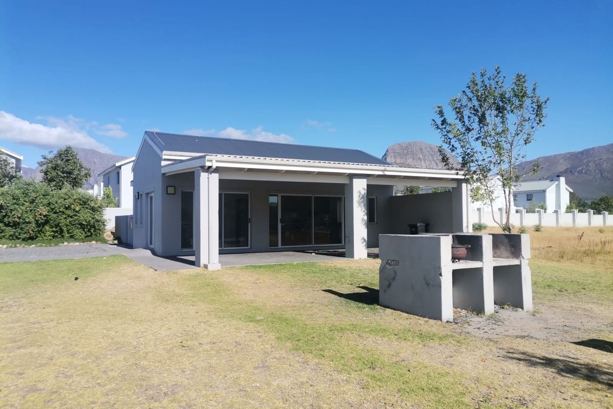 Rear view of the property featuring a covered patio area and a built-in concrete braai, set against a mountain backdrop.