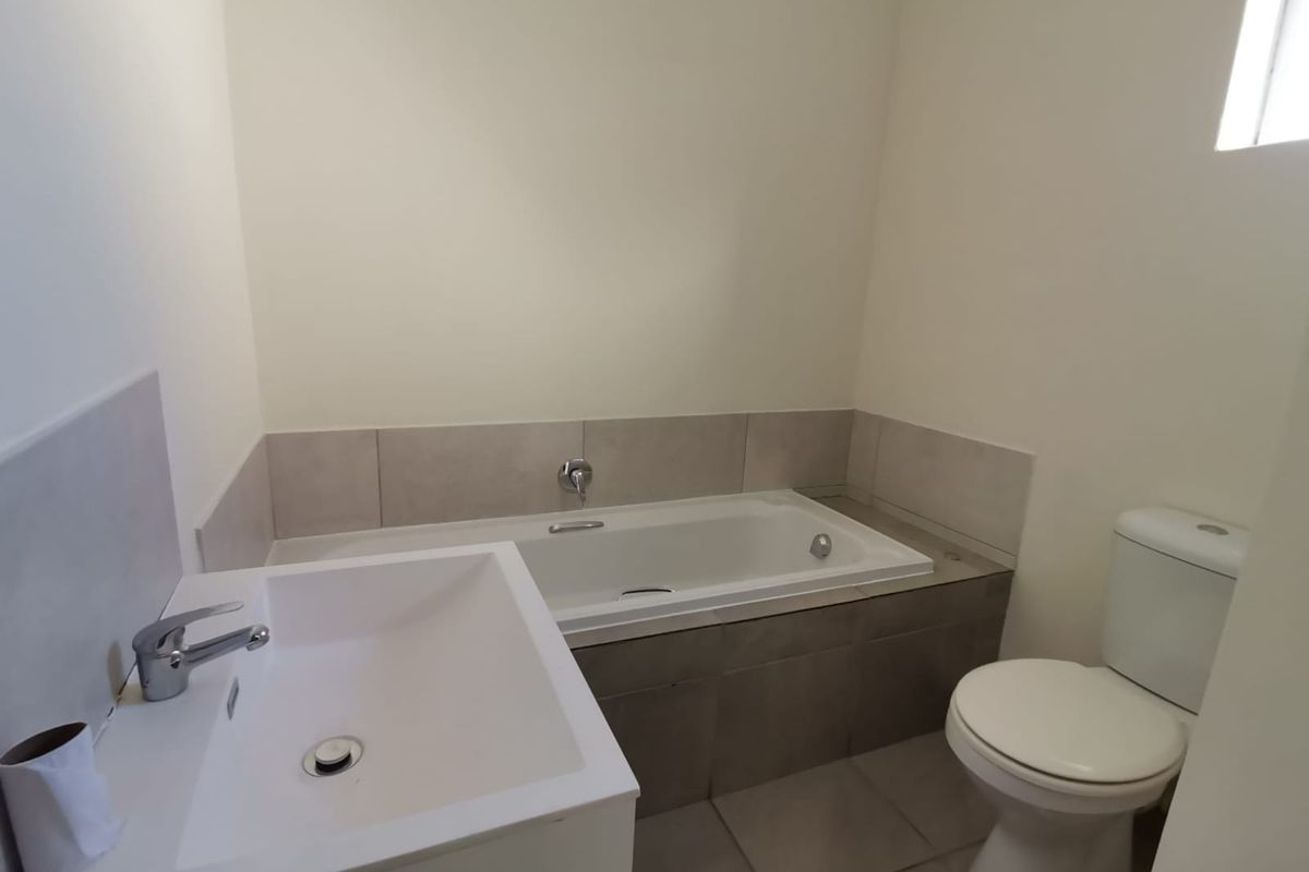 A clean, modern bathroom featuring a built-in bathtub with tiled surround, a contemporary vanity basin, and a standard toilet.
