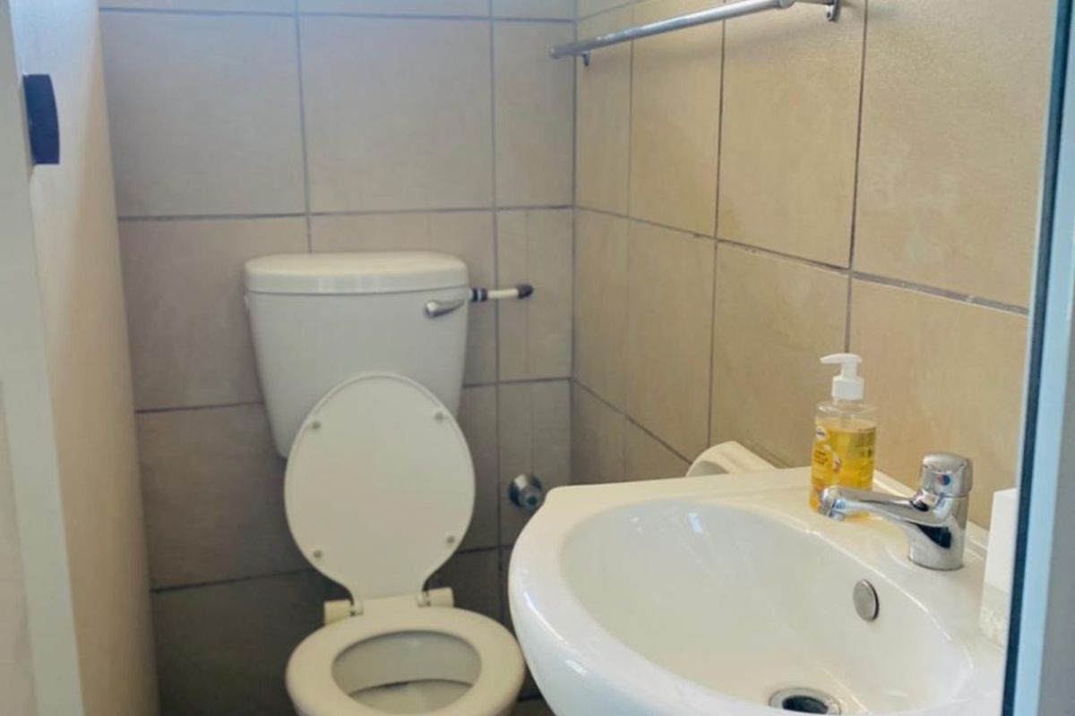 A compact bathroom featuring a pedestal basin, a standard toilet, and neutral wall tiling with a small window for natural light.