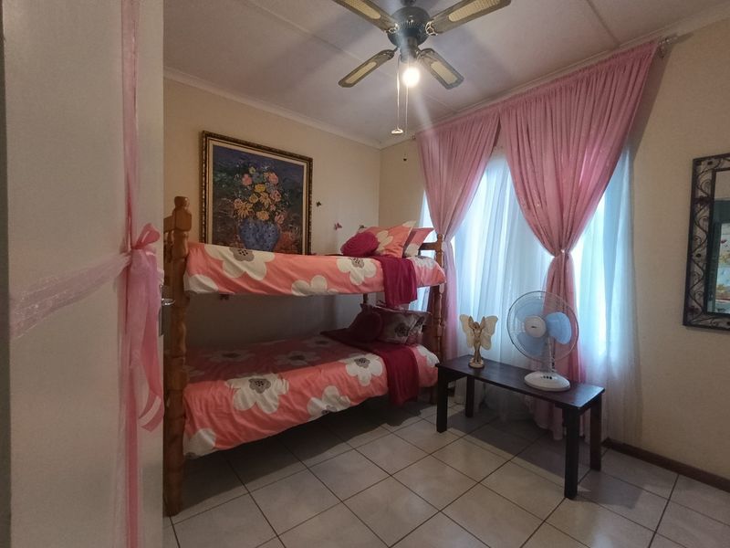 A bedroom featuring tiled flooring and a ceiling fan, with natural light provided by a window dressed with curtains.