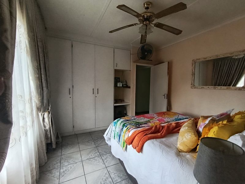 A bedroom featuring built-in cupboards, tiled flooring, and a ceiling fan, offering a functional space with potential for modernization.