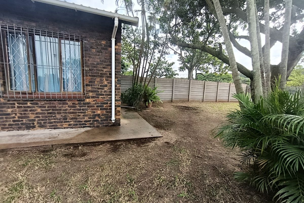 Rear exterior view of the property featuring a face brick facade, security bars on windows, and a large garden area with a precast boundary wall.