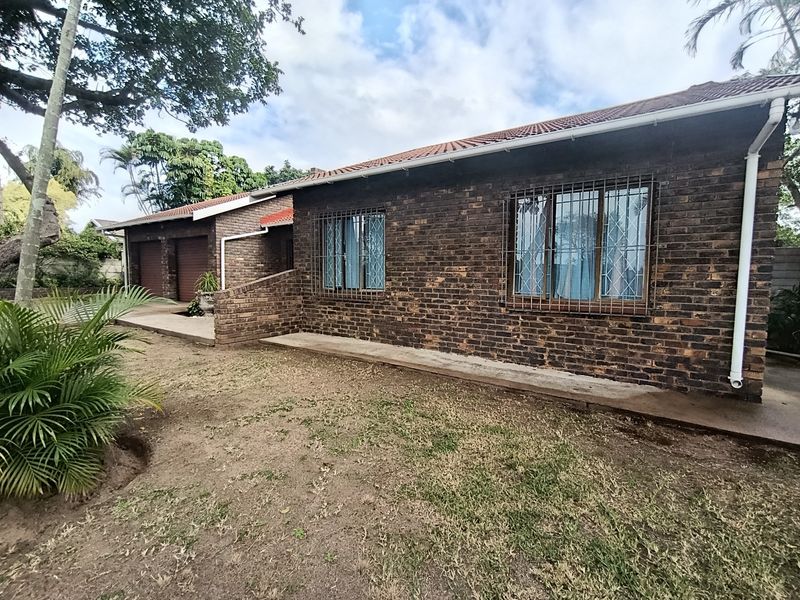 A view of the front exterior of a face brick house featuring a double garage, security bars on windows, and a surrounding garden area.
