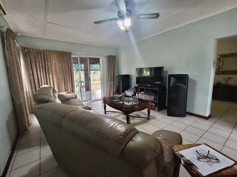 A spacious living room featuring tiled flooring, a ceiling fan, and a sliding glass door providing access to the outdoor area.