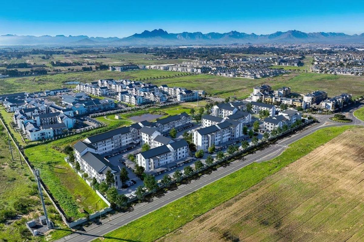 Aerial view of a modern retirement village complex featuring multiple residential buildings, landscaped grounds, and surrounding open fields with mountain views.