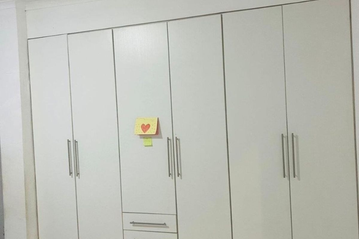 A bedroom featuring a large, white built-in wardrobe with integrated drawers and modern metal handles, set against a tiled floor.
