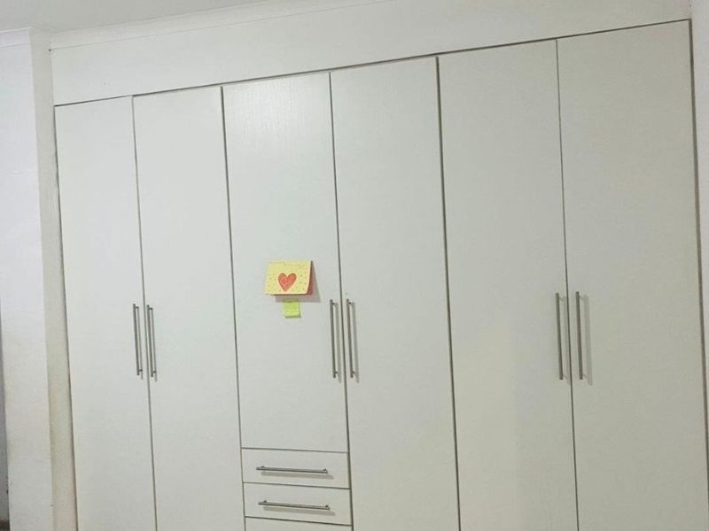 A bedroom featuring a large, white built-in wardrobe with integrated drawers and modern metal handles, set against a tiled floor.
