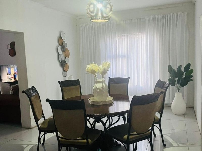 A bright dining room featuring neutral tiled flooring and a central pendant light fixture, providing a clean and functional space for meals.