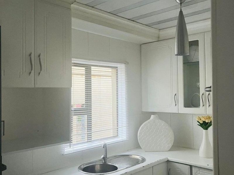 A compact kitchen featuring white cabinetry, a stainless steel sink, and a modern metallic ceiling finish.