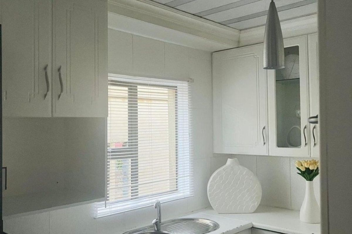 A compact kitchen featuring white cabinetry, a stainless steel sink, and a modern metallic ceiling finish.