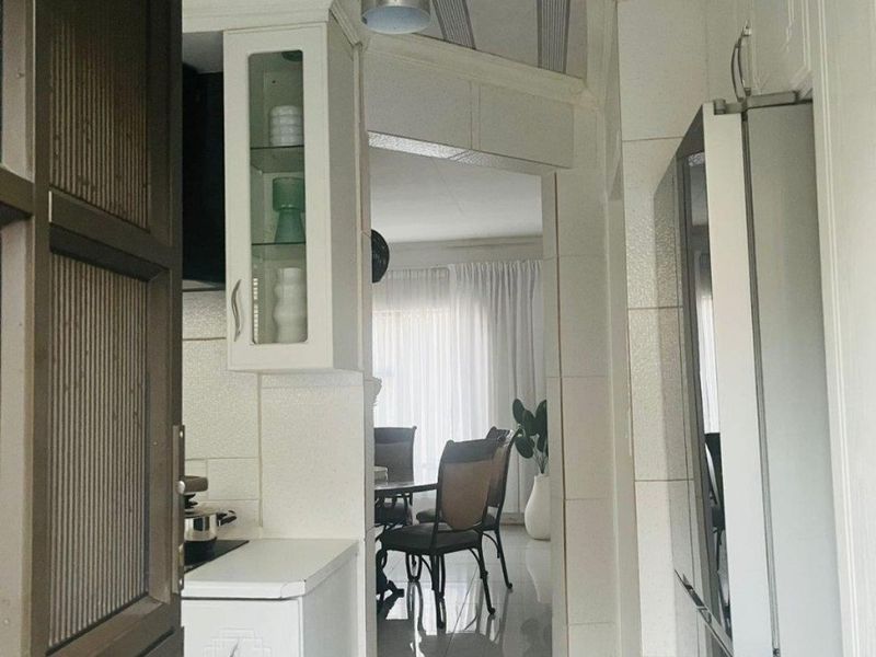 A compact kitchen area featuring white cabinetry and tiled flooring, providing a functional transition space leading into the dining area.