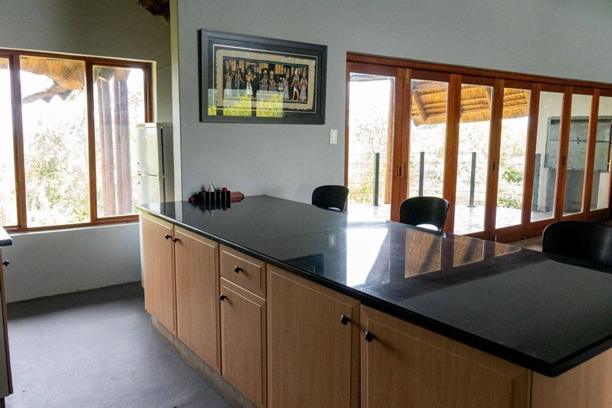 A kitchen area featuring a large central island with dark stone countertops, light wood cabinetry, and large glass sliding doors leading to an outdoor space.