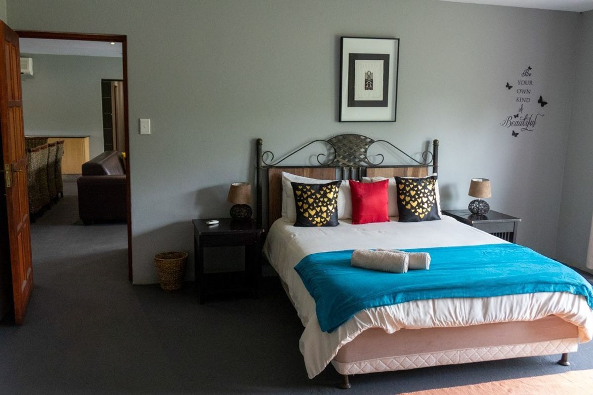 A spacious bedroom featuring neutral wall tones, carpeted flooring, and a doorway leading to an adjacent living area.