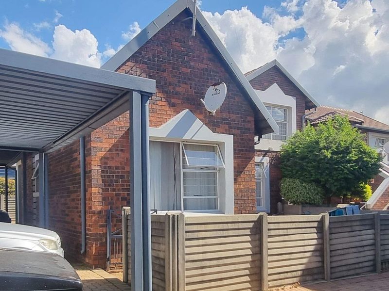 Front exterior view of a brick townhouse featuring a covered carport, paved driveway, and a private fenced courtyard area.
