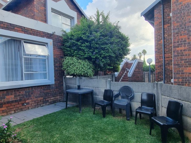 A private rear garden area featuring a small lawn, paved walkway, and concrete boundary wall, adjacent to the townhouse exterior.