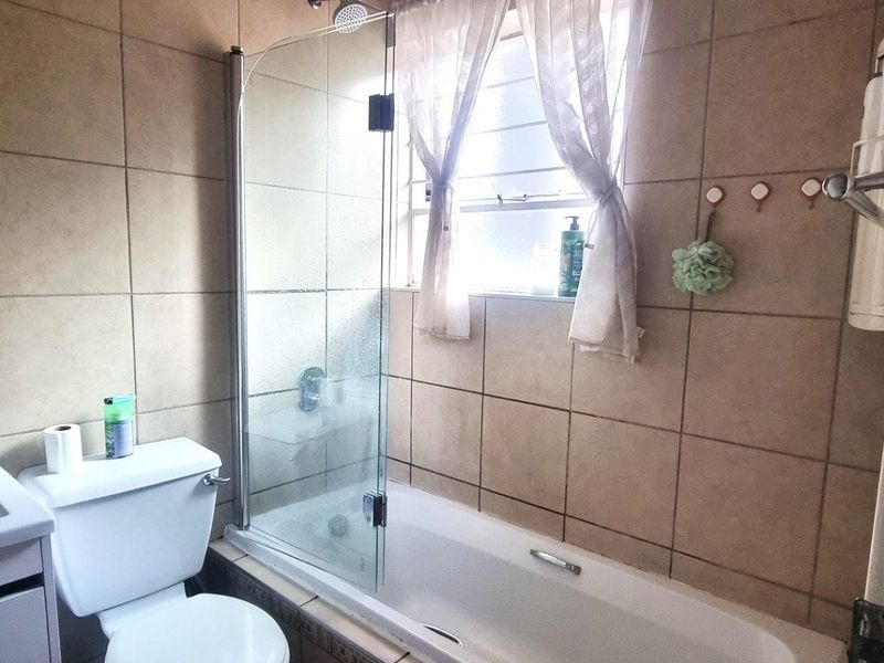A functional bathroom featuring a combined shower and bathtub with a glass screen, tiled walls, and a vanity basin.