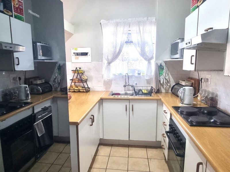 A functional U-shaped kitchen featuring laminate countertops, built-in electric hobs, ovens, and overhead extractor fans with tiled flooring.