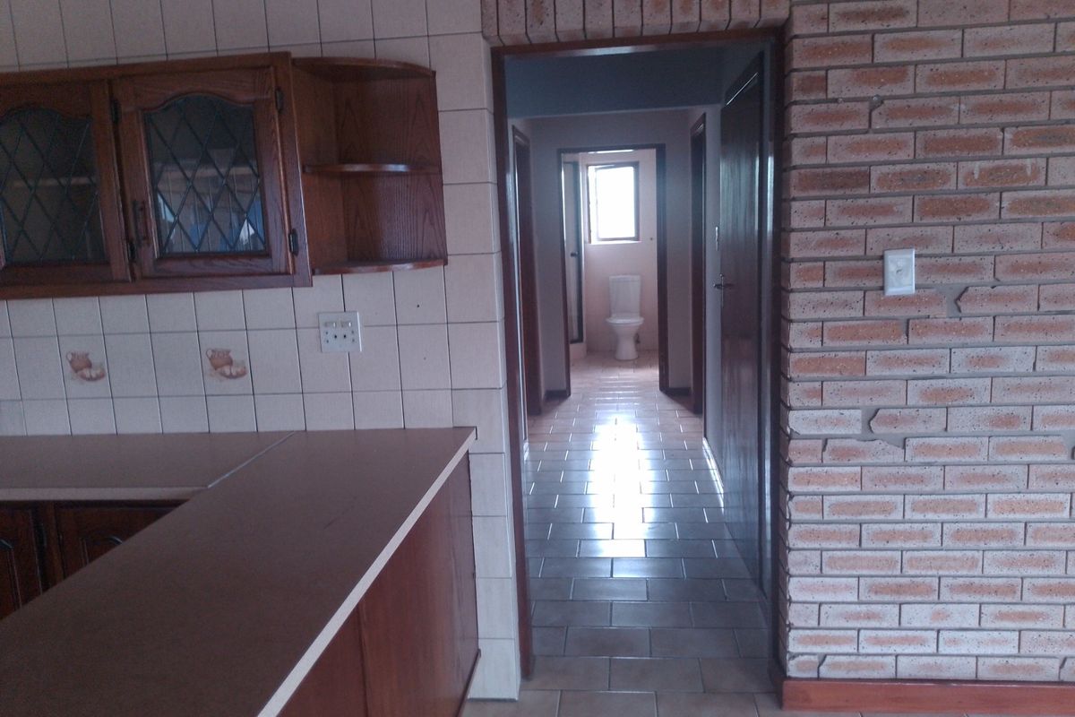 Kitchen area featuring dated wooden cabinetry and exposed brickwork, leading into a tiled hallway with a view towards a bathroom.