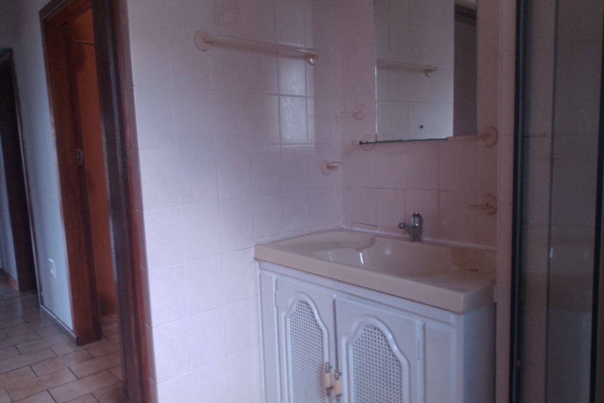 A dated bathroom featuring a vanity cabinet with a basin, wall-mounted mirror, and tiled walls.