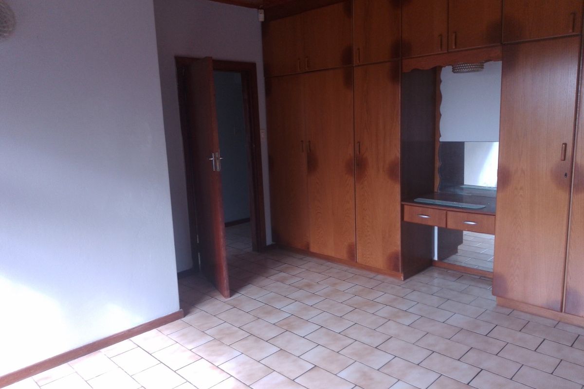 A bedroom featuring extensive built-in wooden cupboards with an integrated vanity, tiled flooring, and a timber-paneled ceiling.