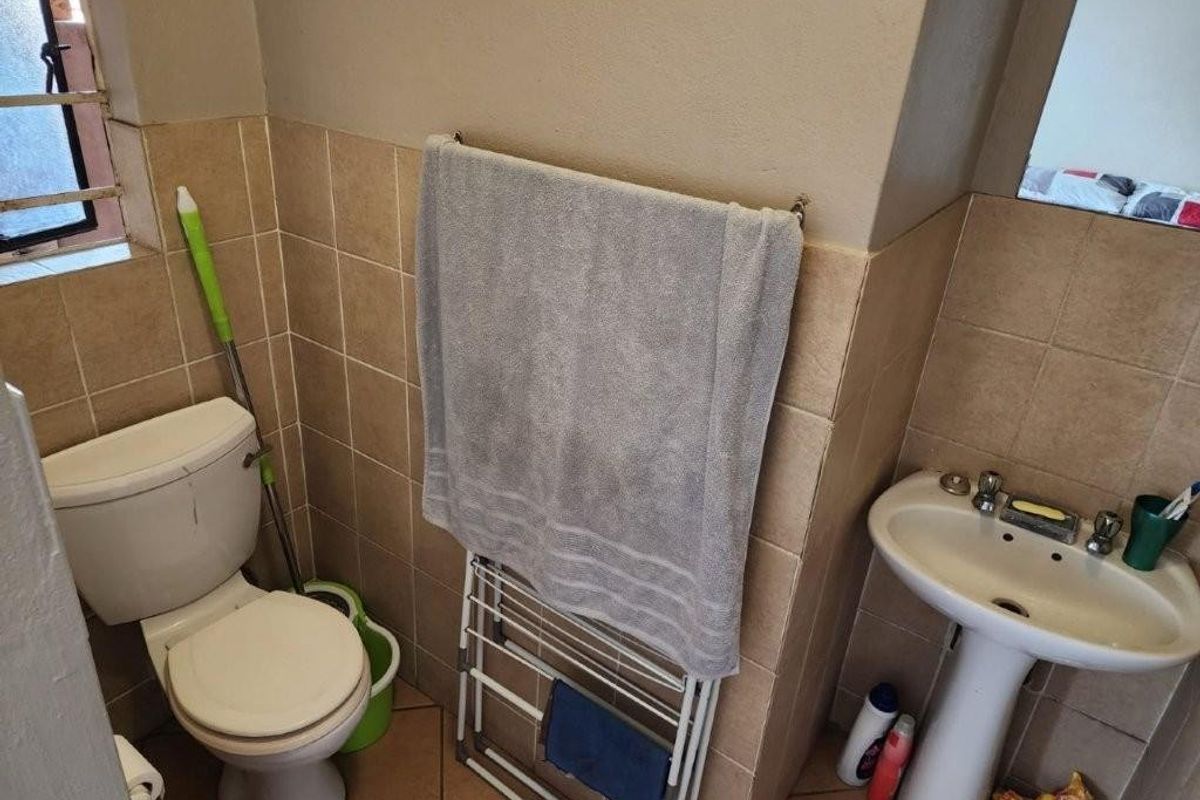 A functional bathroom featuring a pedestal basin, a standard toilet, and tiled walls and flooring.