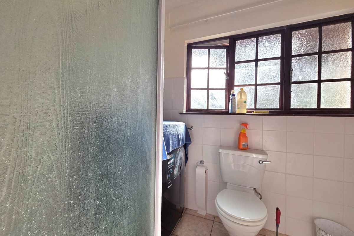A functional bathroom featuring a toilet, tiled walls, and a shower enclosure with textured glass, illuminated by natural light from a multi-pane window.