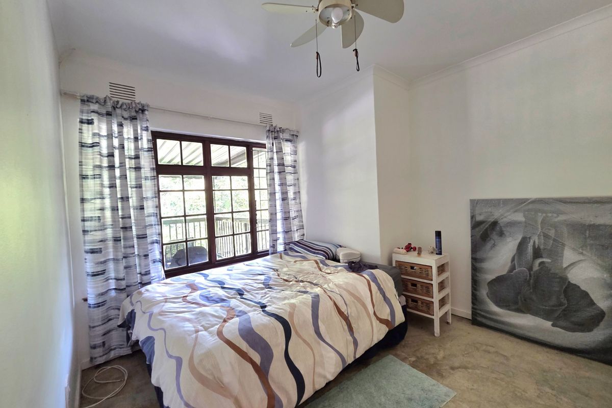 A bedroom featuring a ceiling fan, large window with garden views, and exposed concrete flooring, offering a blank canvas for potential updates.