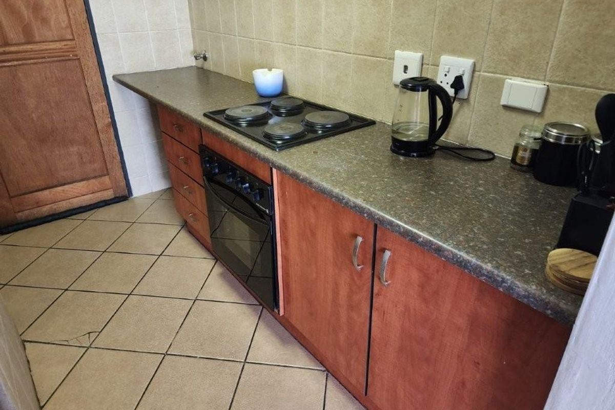 A functional kitchen featuring laminate countertops, built-in oven, electric hob, and tiled splashbacks with ceramic floor tiling.