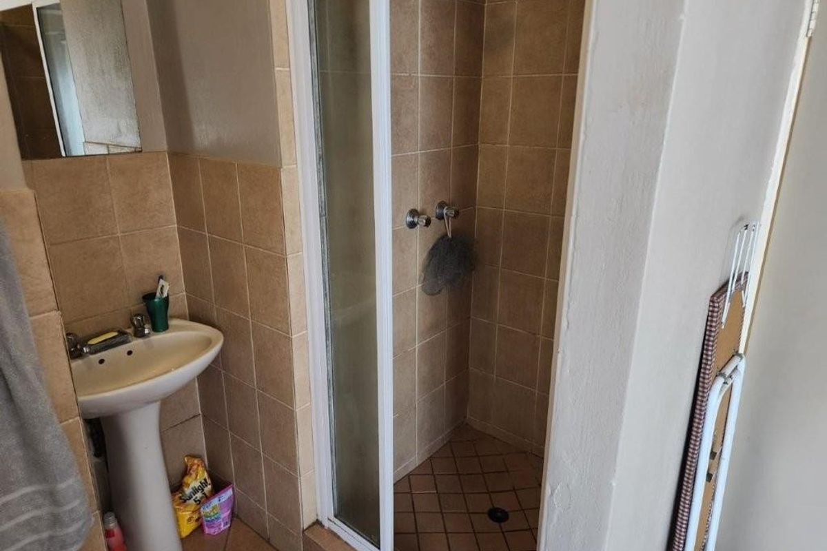 A functional bathroom featuring a pedestal basin, a tiled shower enclosure with a glass door, and neutral wall tiling.