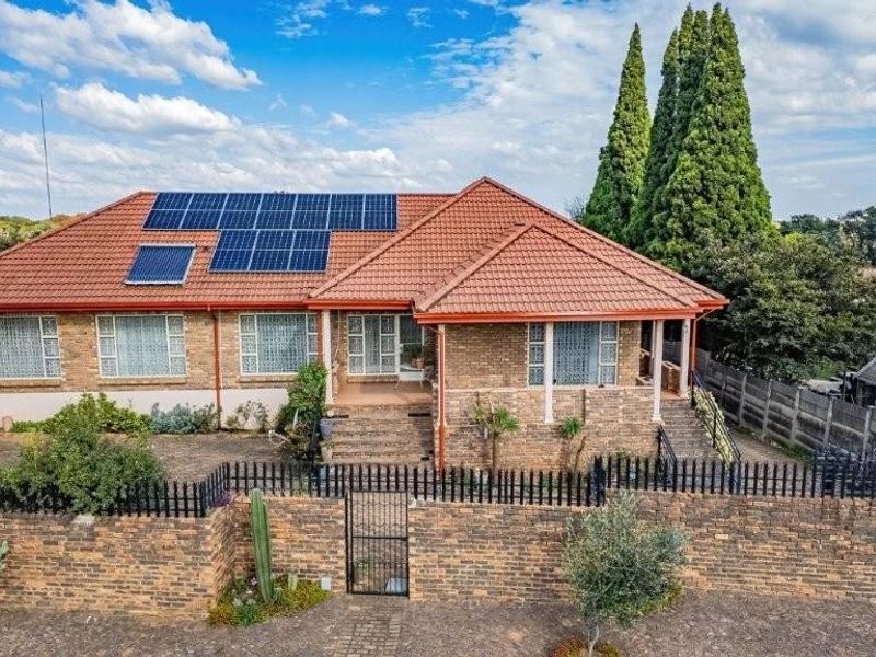 A well-maintained single-story brick house featuring a tiled roof, solar panels, and a secure perimeter wall with gated access.