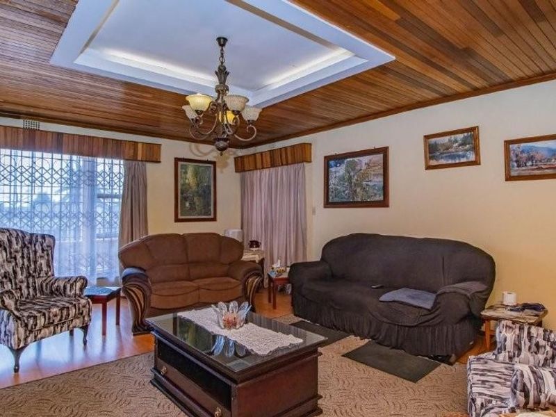 A spacious living room featuring a distinctive timber-paneled ceiling with recessed lighting and large windows secured with decorative metal security grilles.
