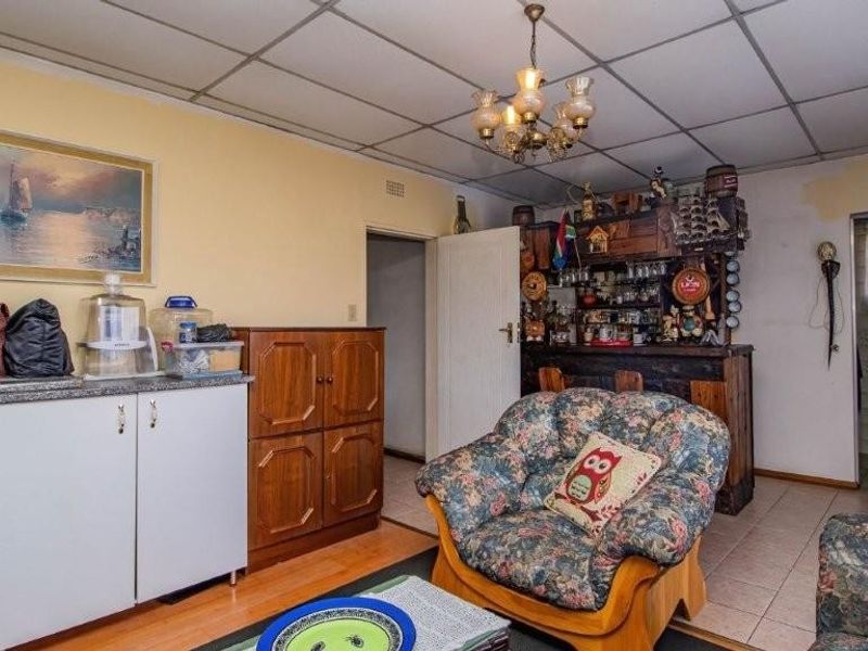 A dated living area featuring a built-in wooden bar, drop ceiling tiles, and tiled flooring, offering potential for modernization and renovation.