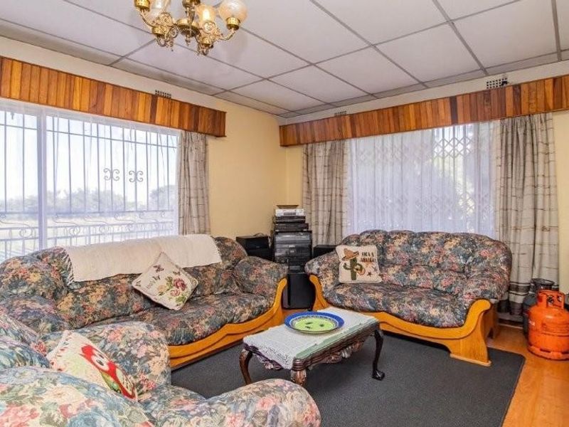 A living room featuring wood paneling, drop ceiling tiles, and large windows with security bars, offering a dated aesthetic ready for modernization.